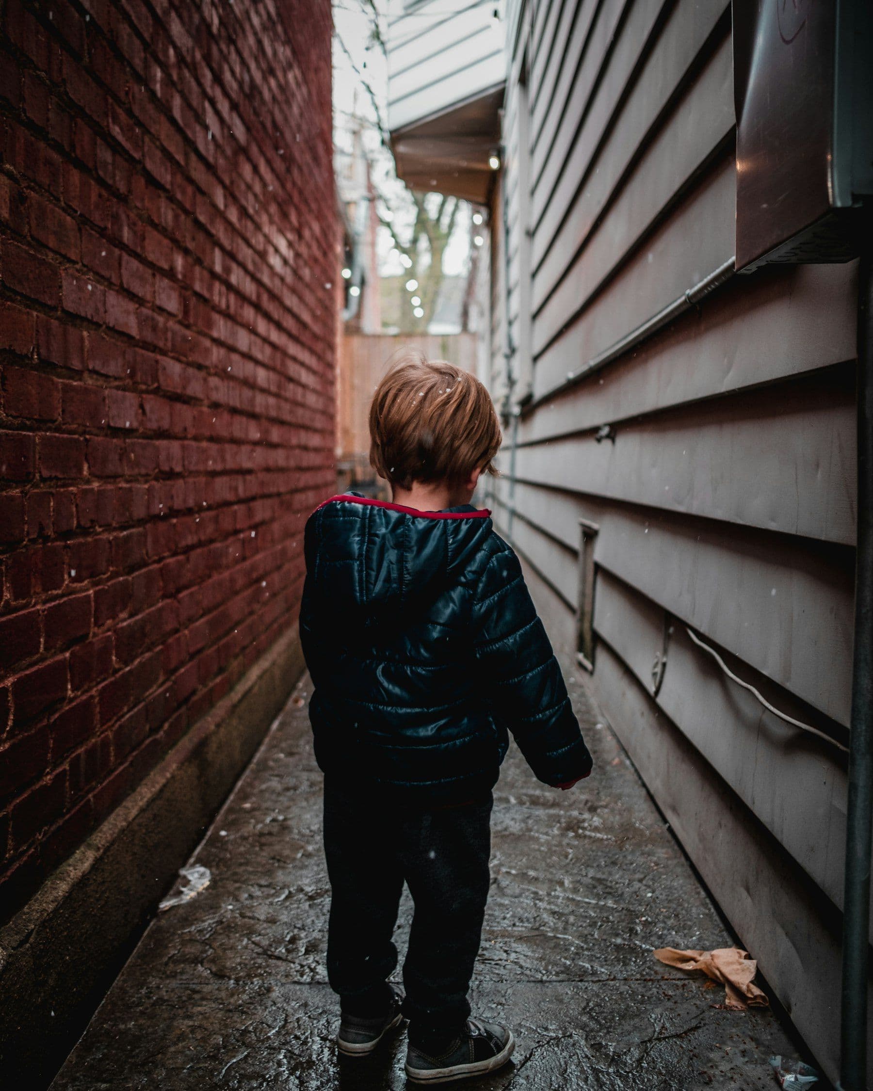 Toddler in an alley, turned partly away, capturing reflection and quiet resolve.