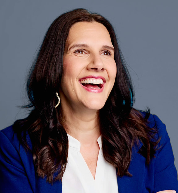 Amy Kirkland laughing against a subdued blue-gray backdrop.